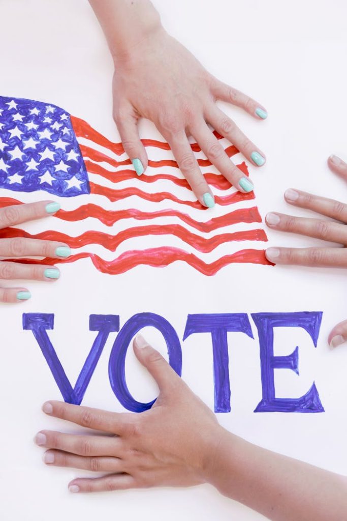 Hands reaching for American flag banner with VOTE text, promoting democratic participation.
