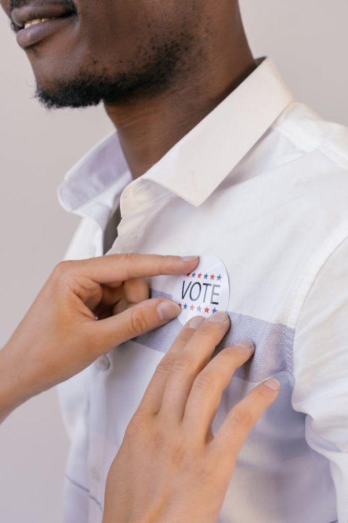 Hands placing a vote button on a shirt symbolizing participation in democracy.